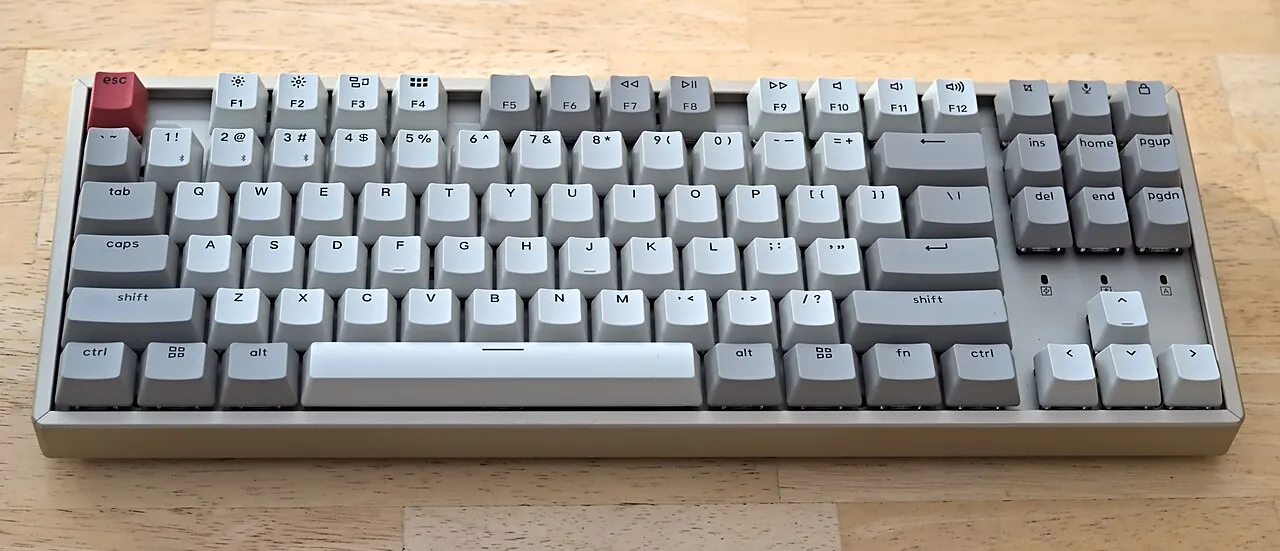 Clavier mécanique gris et blanc posé sur un bureau en bois