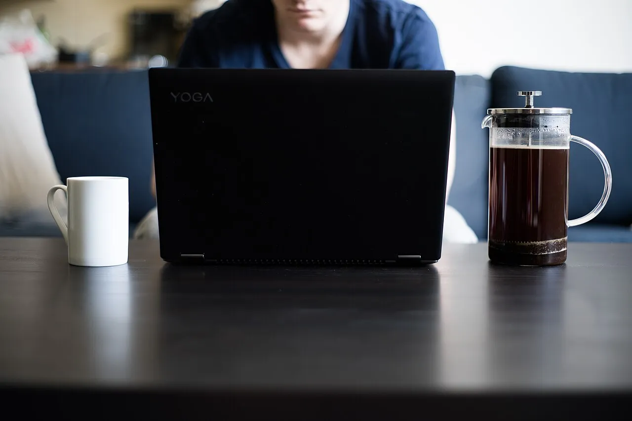 Ordinateur portable fermé à moitié sur une table, entre une tasse et une cafetière