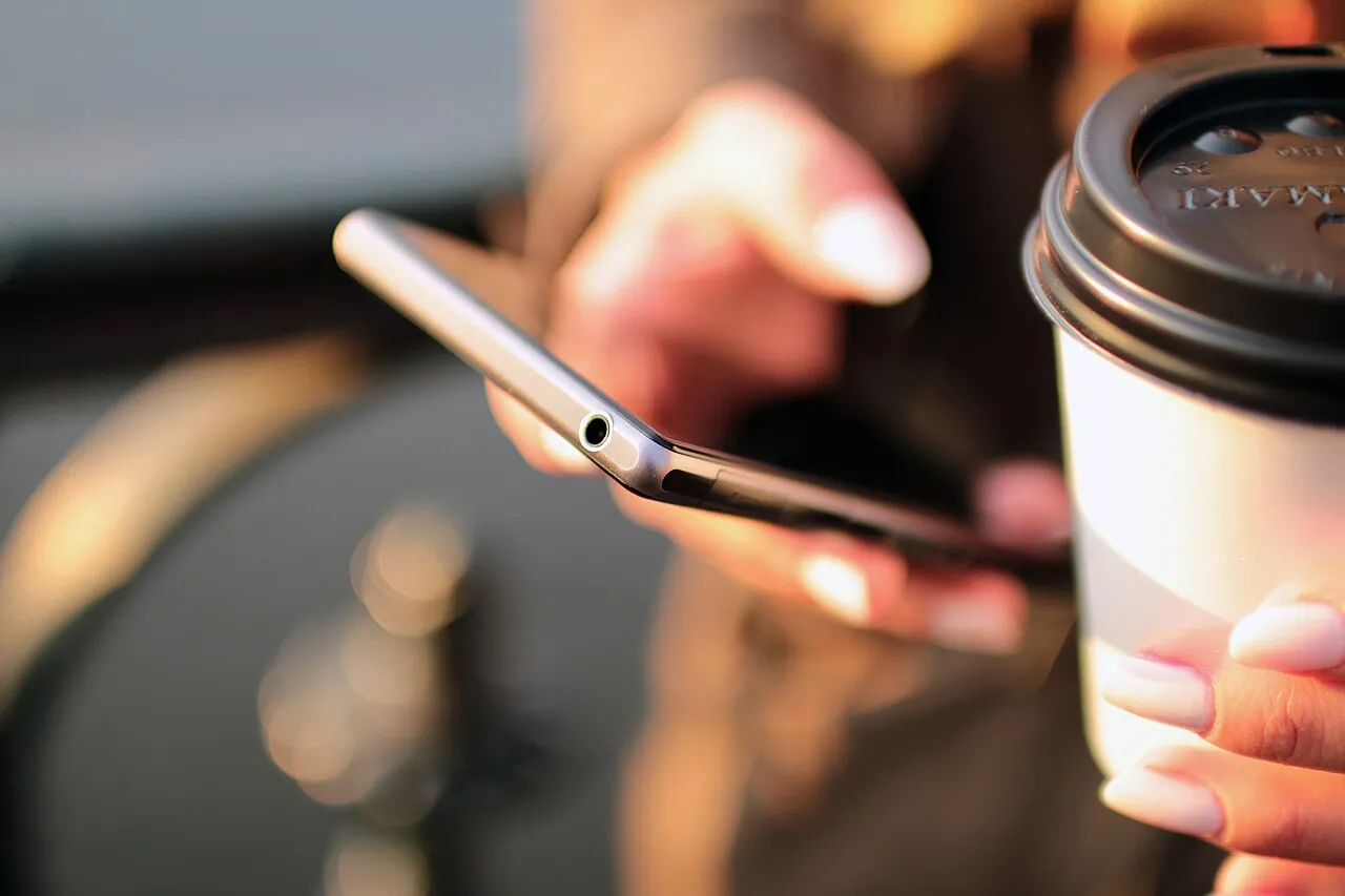 Main tenant un smartphone à côté d’une tasse de café